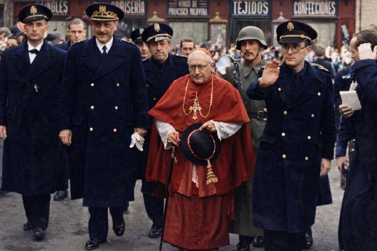 Fotografía histórica coloreada del cardenal Pla y Deniel caminando escoltado por autoridades y militares en una calle de Toledo durante la posguerra.