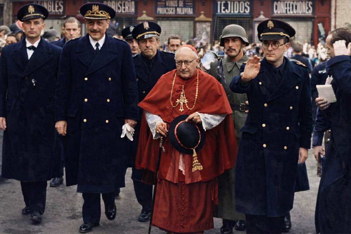 Fotografía histórica coloreada del cardenal Pla y Deniel caminando escoltado por autoridades y militares en una calle de Toledo durante la posguerra.