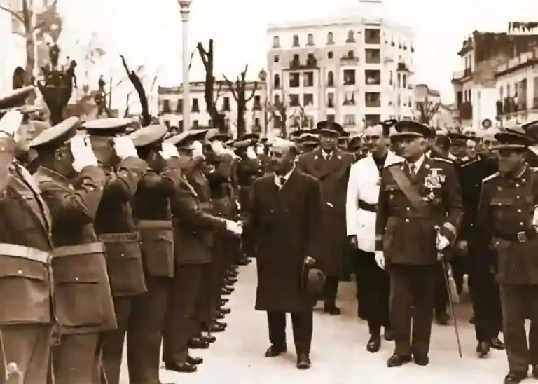 Desfile militar en Córdoba en 1953: autoridades recorren una formación de soldados que saludan, con edificios históricos al fondo.