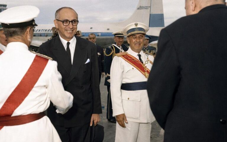 “Fotografía histórica coloreada de una despedida oficial en el aeropuerto de Barajas en 1960, con autoridades españolas y argentinas junto a un avión de línea.”