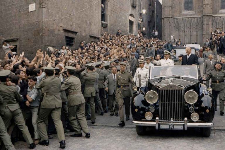 “Fotografía histórica coloreada de una visita institucional a la Ciudad Universitaria de Pedralbes en 1960, con un coche oficial rodeado de autoridades, fuerzas de seguridad y público.”
