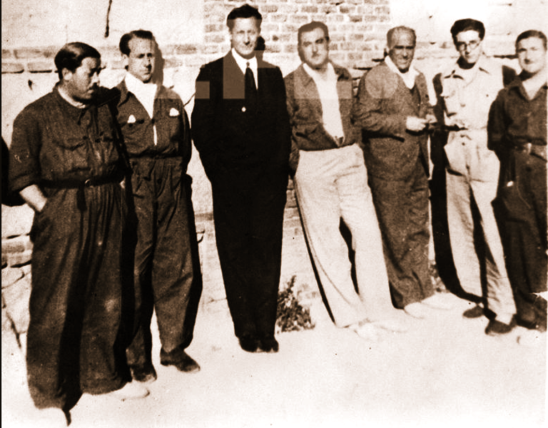 Fotografía histórica en blanco y negro de varios militantes falangistas y simpatizantes posando juntos ante un muro de piedra y ladrillo durante los años treinta.