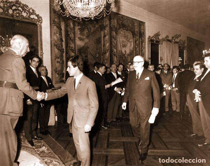 Francisco Franco saludando a un joven durante la entrega de premios de los concursos nacionales de formación profesional, industrial y de artesanía en 1958, en un salón oficial con autoridades y participantes presentes.