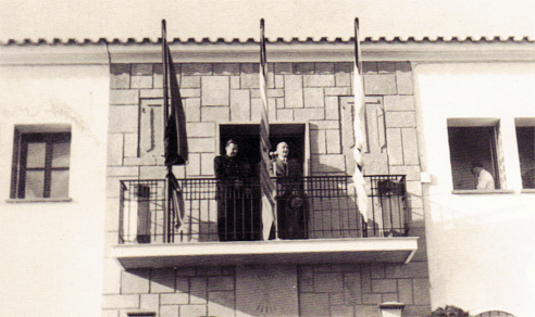 Francisco Franco en el balcón del Ayuntamiento de Marmolejo durante un acto oficial en 1961, con banderas ondeando sobre la fachada del edificio en una fotografía histórica colorizada.