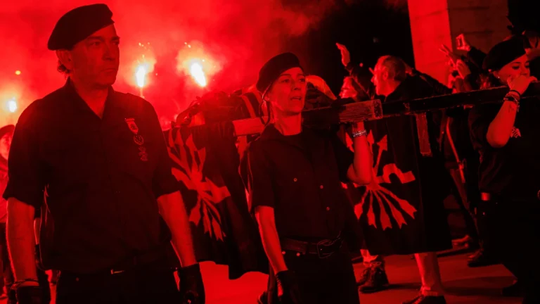 Militantes de Falange Española portando una cruz y banderas durante un acto nocturno con bengalas rojas en Madrid, en una imagen relacionada con homenajes políticos y la Ley de Memoria Democrática en España.