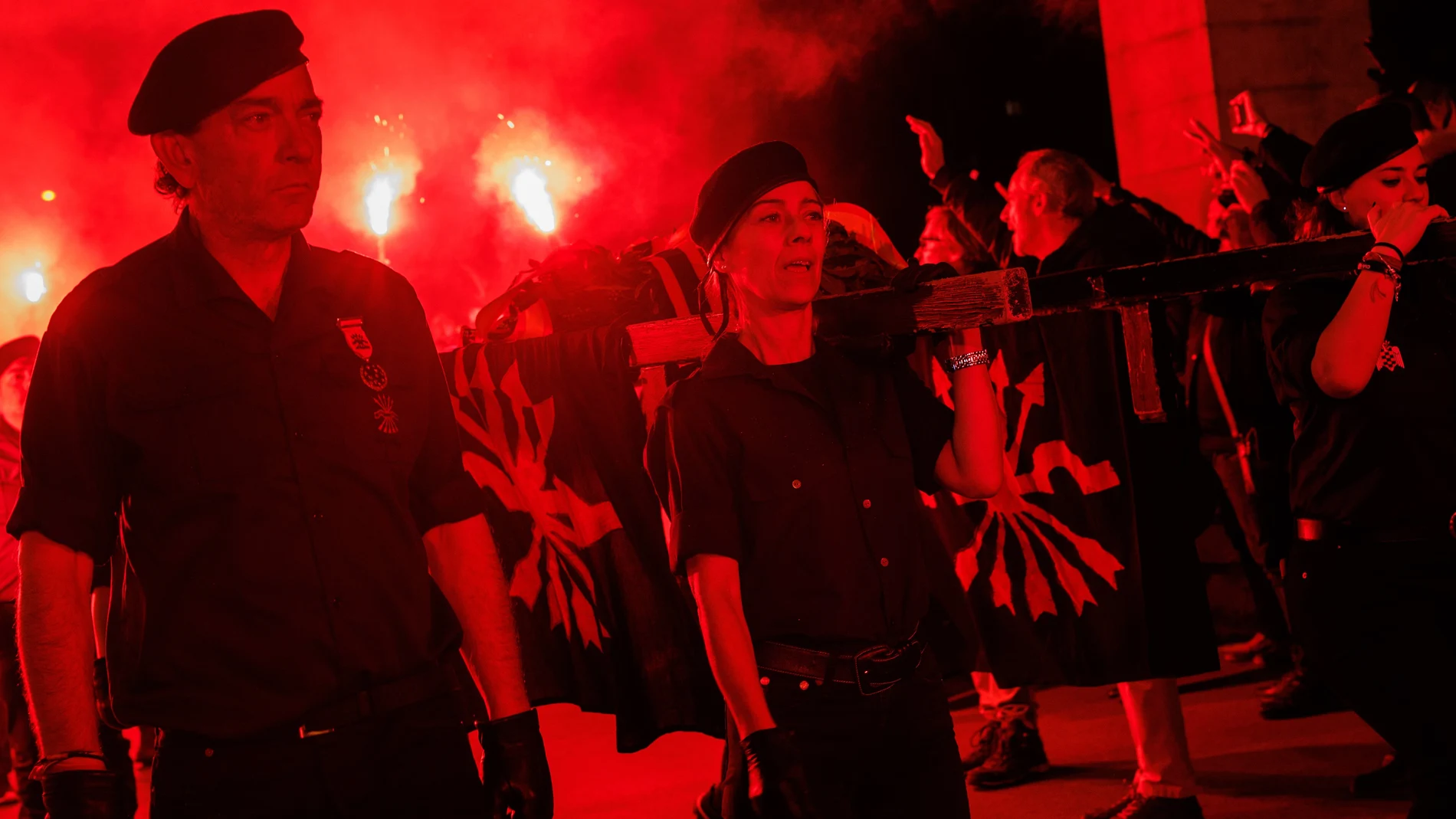 Militantes de Falange Española portando una cruz y banderas durante un acto nocturno con bengalas rojas en Madrid, en una imagen relacionada con homenajes políticos y la Ley de Memoria Democrática en España.